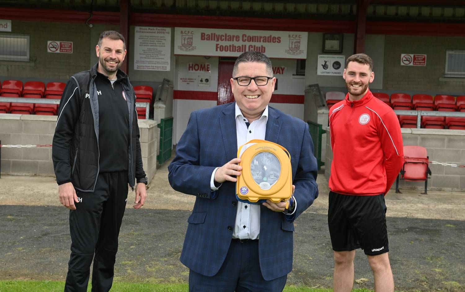 NIFL Chairman Gerard Lawlor presents a defibrillator to Ballyclare Comrades manager Paul Harbinson and player Kyle Crawford