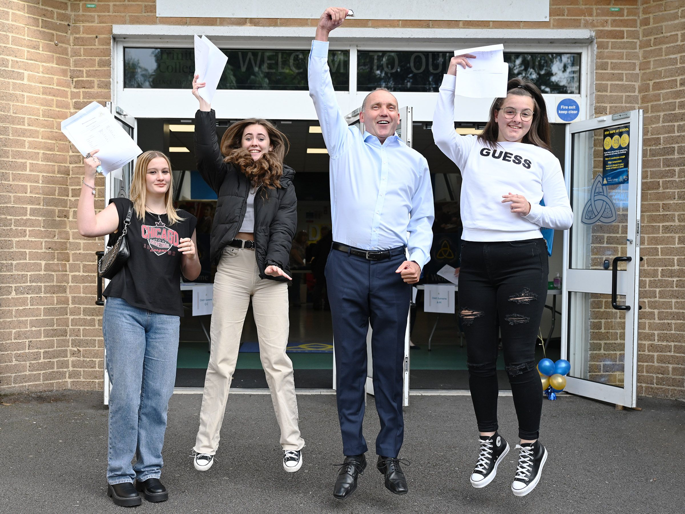 JUMP FOR JOY: Blessed Trinity College GCSE students Rhiannon O\'Neill, Jenny Crawford and Aimee Bowman with Principal Jim McKeever