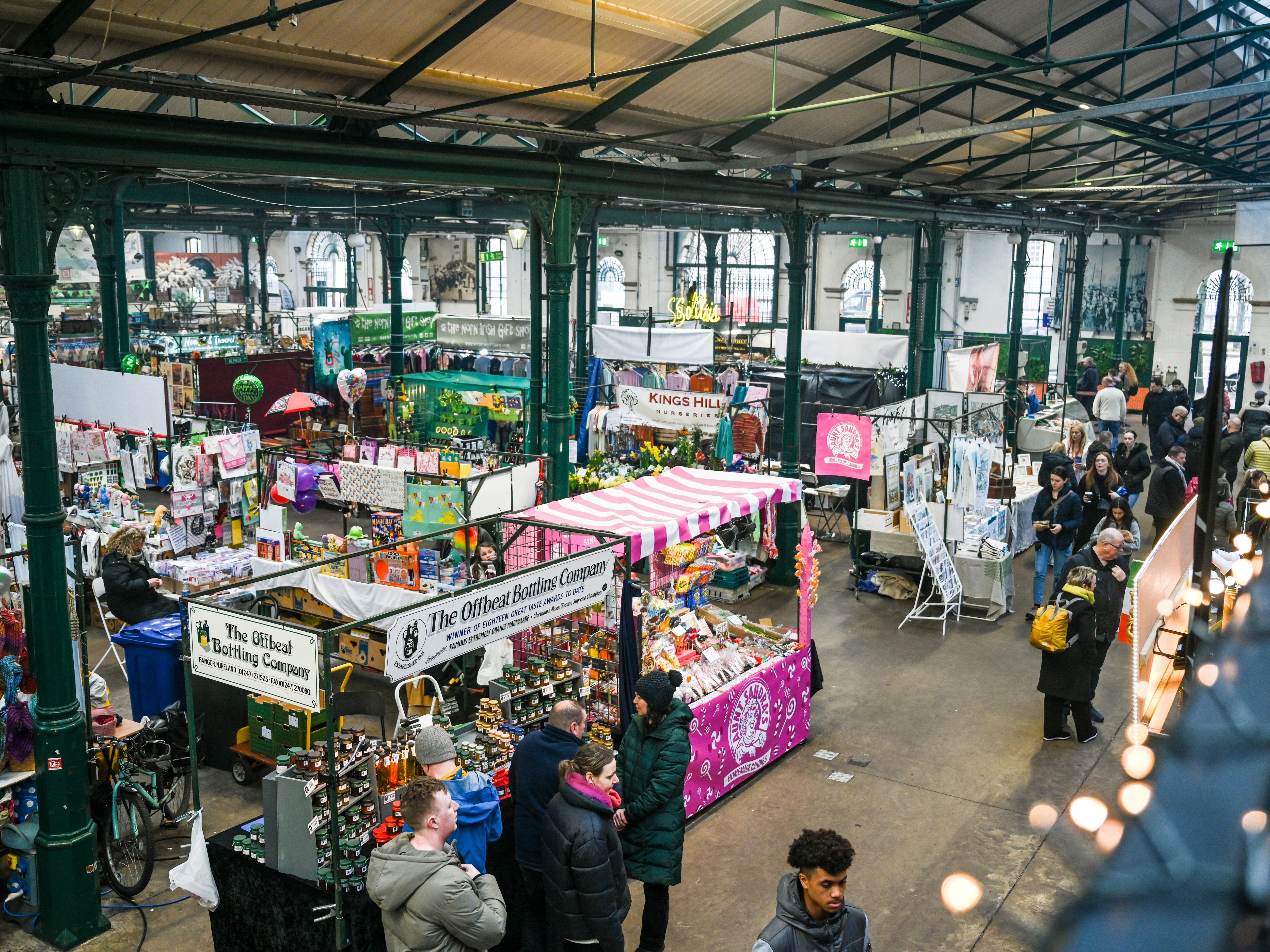 The bustling interior of St. George's Market in Belfast, with vendors selling various goods and people milling about under a high arched ceiling.