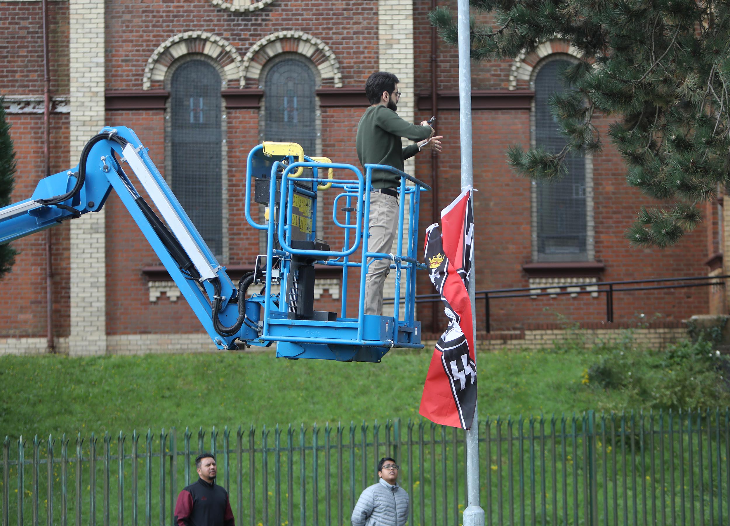 RACE HATE: The three fascist flags featuring Nazi symbols were erected last night. Above a member of the Mosque removes them.