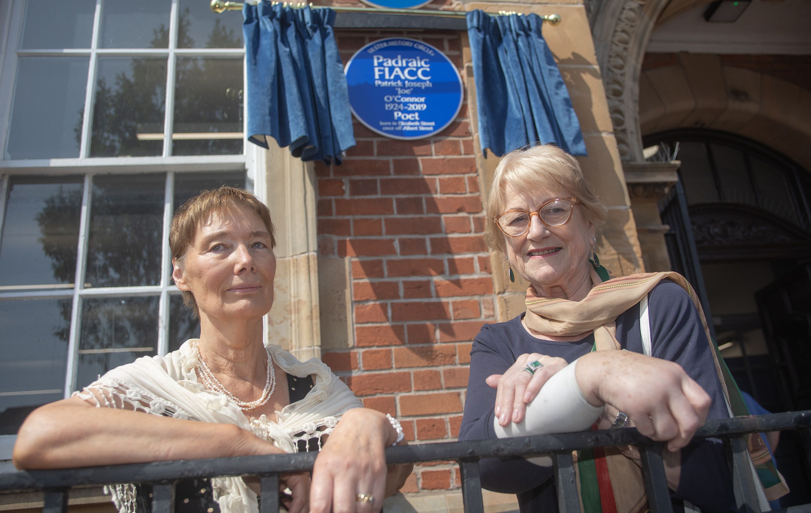 WAR POET HONOURED: Áine Andrews (wife of the late Aodán Mac Póilín) and Dorothea Melvin (wife of the late Gerald Dawe) unveil the blue plaque on Falls Road Library