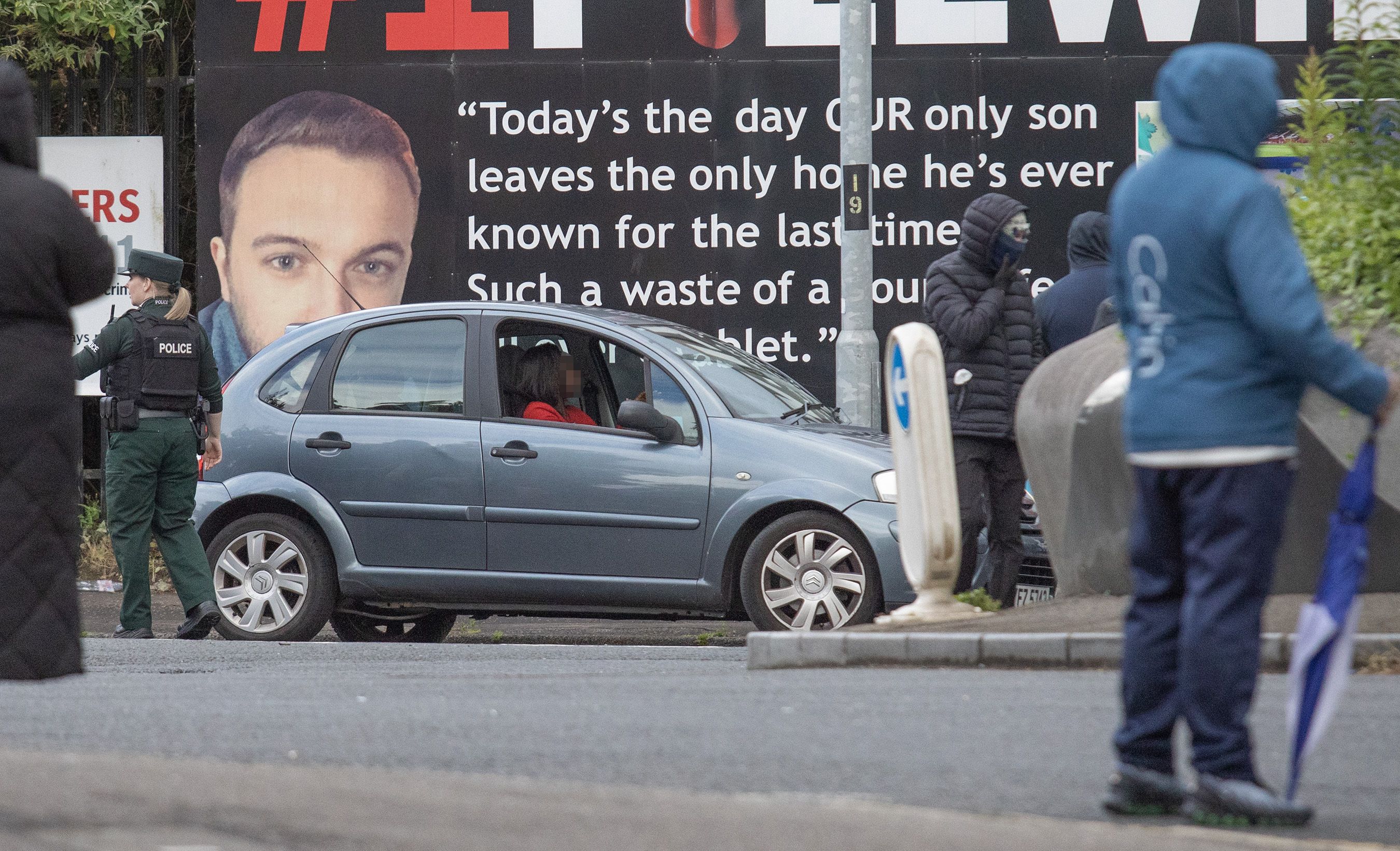 TERROR ON STREETS: A black woman is stopped at a \'roadblock\' by masked men as PSNI look on in North Belfast. The driver was turned back by the protesters