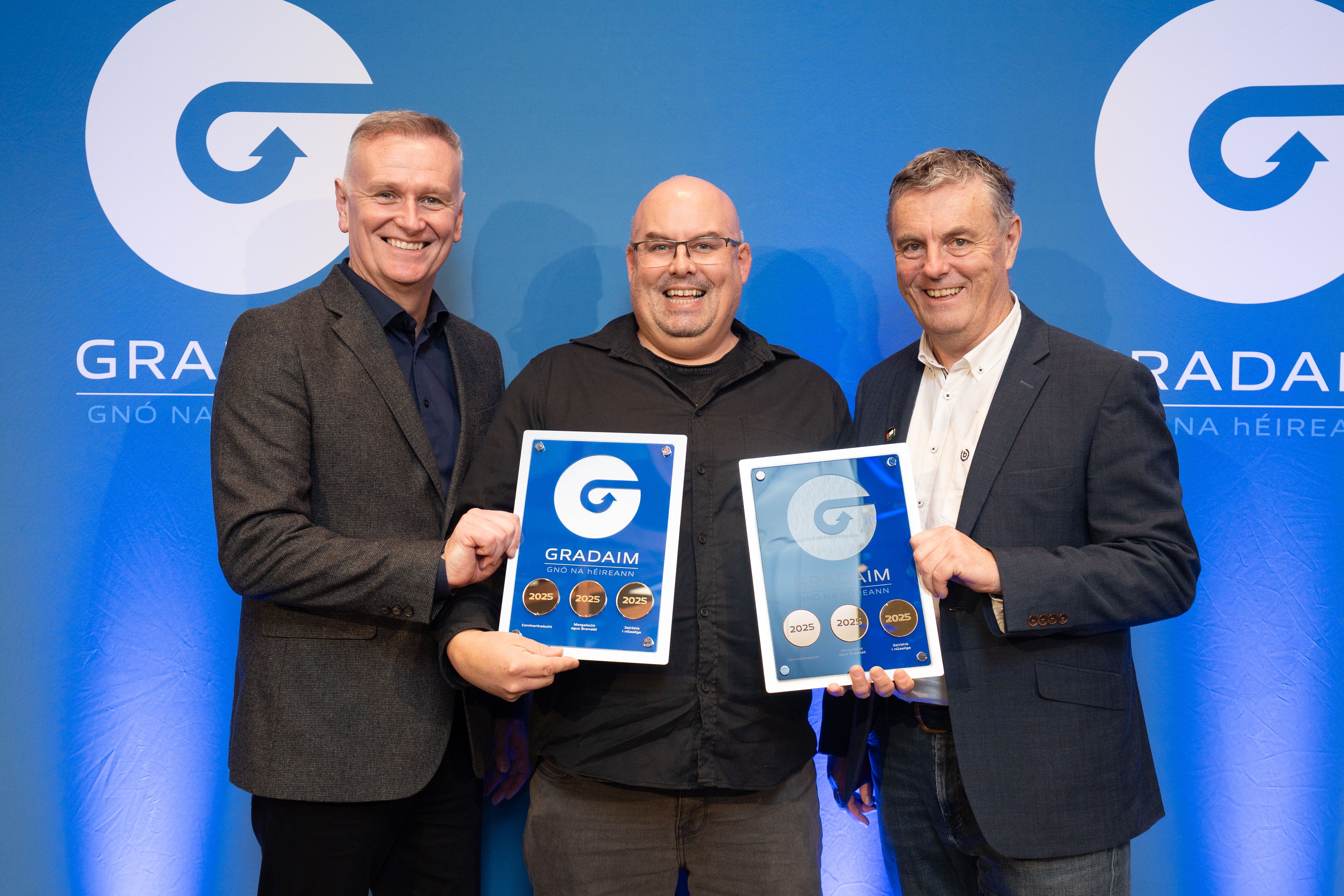 Cillian Breatnach receiving Gradaim Gnó na hÉireann awards on behalf of Raidió Fáilte and An tÁisaonad, from Daithí Ó Sé and Lorcán Mac Gabhann