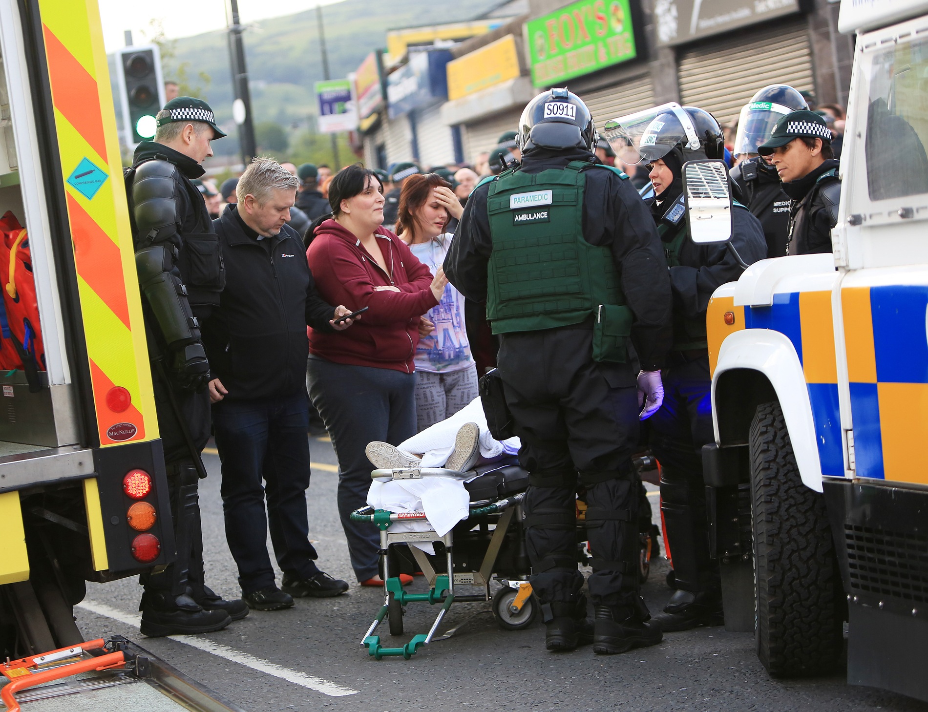 Distressed relatives look on as a 16-year-old girl is taken to an ambulance after being trapped under a car at Ardoyne yesterday. With them is Father Gary Donegan 