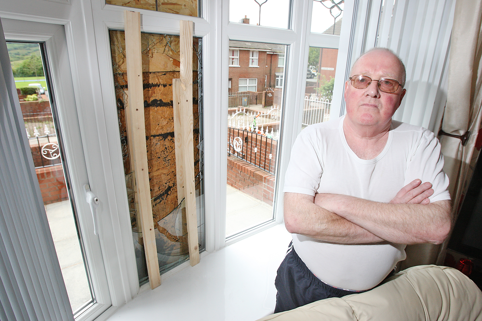 Joe Deans beside the shattered window at his house in Flaxton Place, Ligoniel