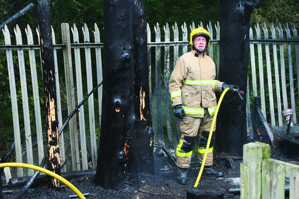 A firefighter feels the heat as he finishes the job of extinguishing a fierce blaze near homes in Merrion Park in Dunmurry – the second deliberate fire at exactly the same spot in the space of a week
