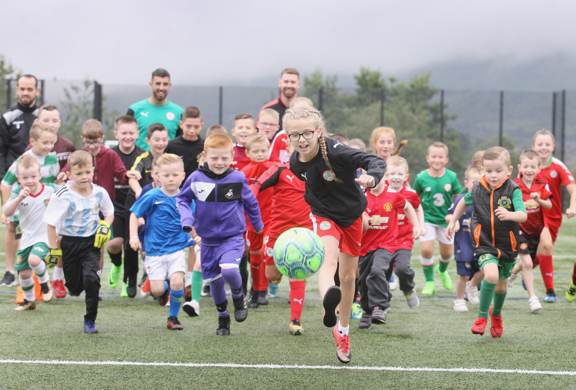 Lucy Loughens kicks off the Mini-World Cup at the Bone Hills pitches as part of the Ardoyne and Bone Festival. Looking on are a number of top Irish League players who gave up their time to come along and pass on some valuable coaching tips