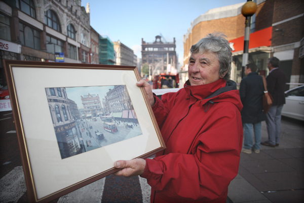 Roberta Johnston on High Street holds a painting of Bank Buildings, while behind her the Primark fire at the famous building is being doused by firefighters this morning