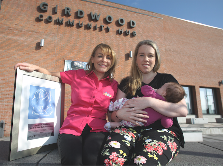 Midwife Mairead Mulligan from Sure Start with Fiona George and baby Fionnla at Girdwood Community Hub with the UNICEF award that Sure Start received for Baby Friendly