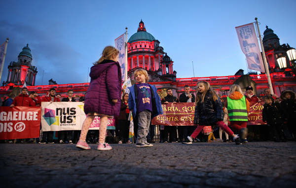 Children laugh and play while the City Hall is lit up red in support of Irish language rights