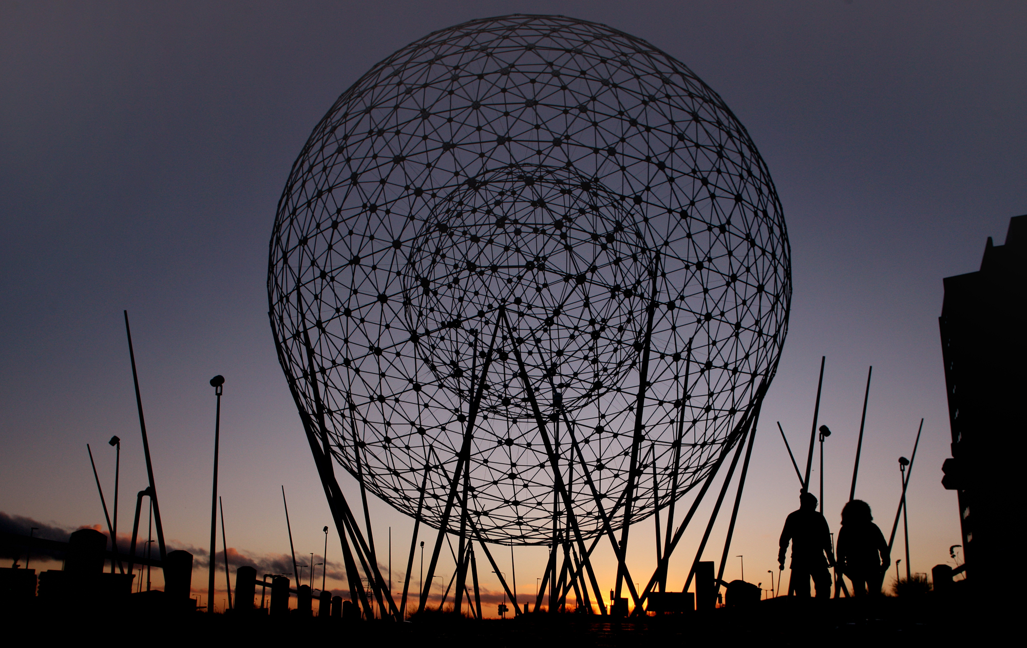 Dusk falls as a couple make their way past the Rise sculpture at Broadway roundabout