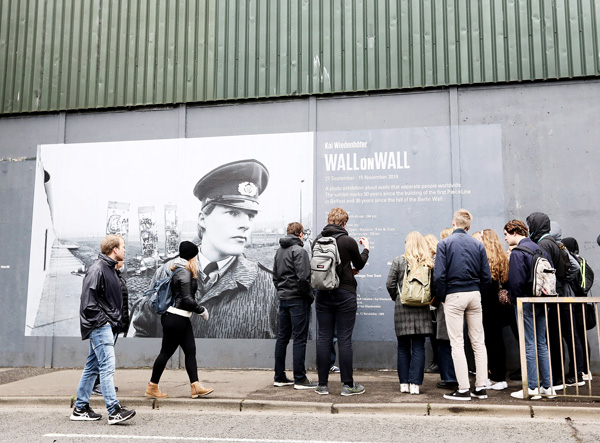 Tourists look at the new art installation at the peace wall on Cupar’s Way in West Belfast entitled Wall on Wall which shows images of the world’s border walls