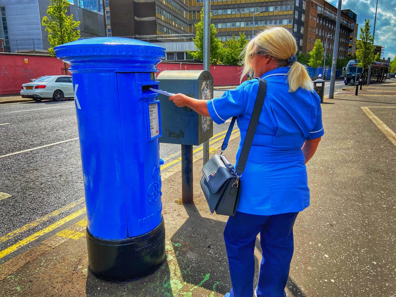 IN THIS TOGETHER:: An RVH worker posts a letter in a post box beside the hospital which has been painted blue as a tribute to health workers. Photo by Thomas McMullan.